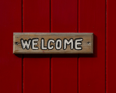 Red wooden door with the word 'welcome' painted in white on a separate wooden board